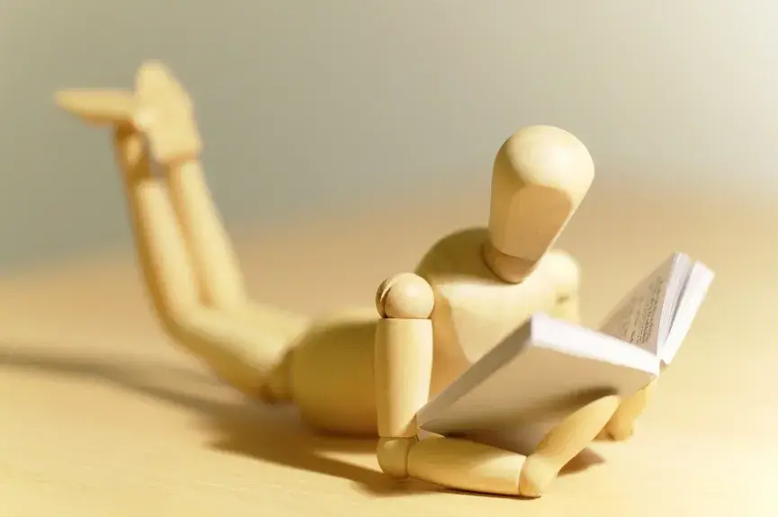 Mannequin en bois allongé sur le ventre un livre ouvert dans ses mains
